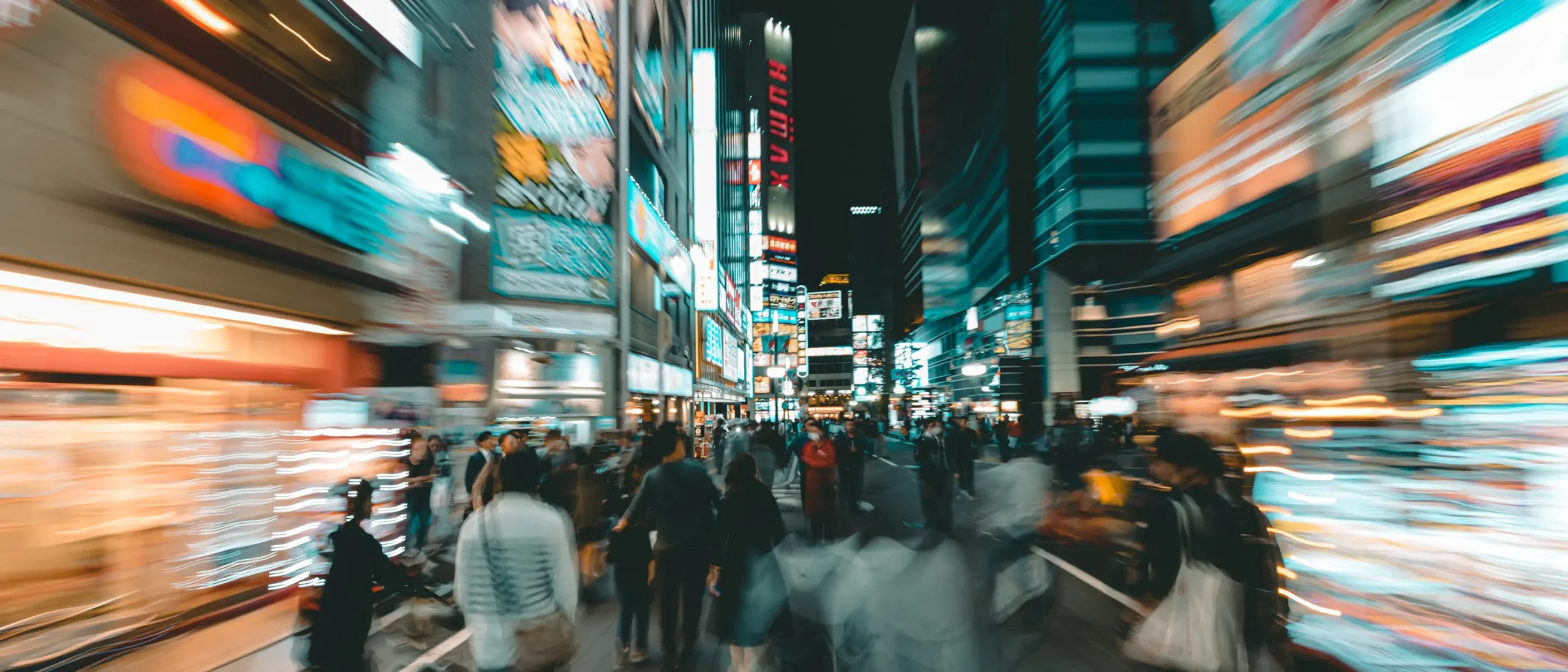 A bustling night city scene with blurred motion effect, showing a crowd of people walking among brightly lit neon signs and billboards, creating a vibrant, energetic atmosphere.